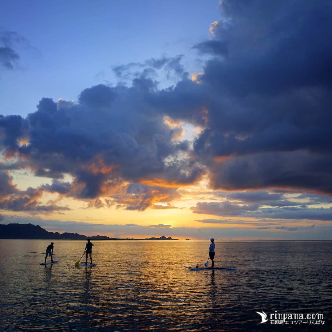 SUPに乗って夕陽を海の上で見る写真